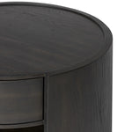 Rich contours bring character to the bedside. A round black-finished oak table has a spacious cubby and a single drawer with metal glides and a bronzed pull Amethyst Home provides interior design, new home construction design consulting, vintage area rugs, and lighting in the Miami metro area.