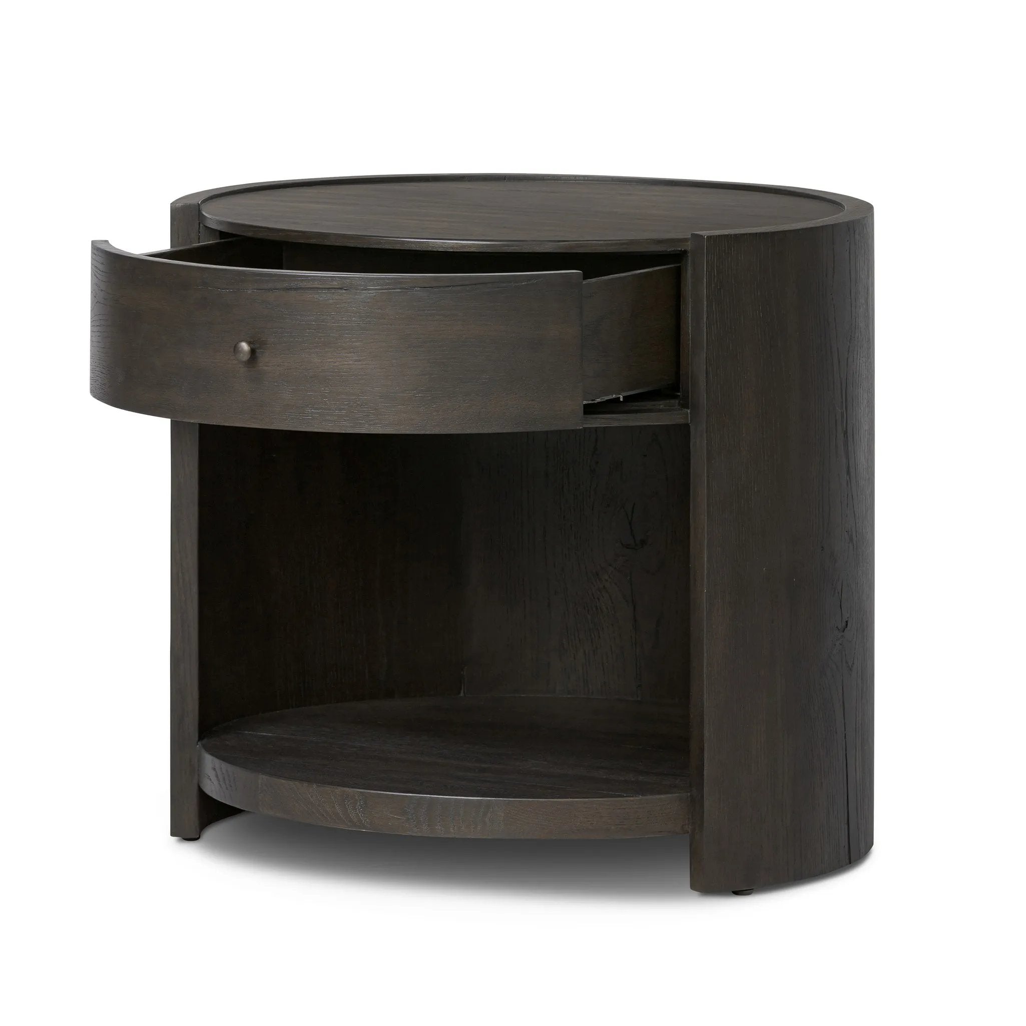 Rich contours bring character to the bedside. A round black-finished oak table has a spacious cubby and a single drawer with metal glides and a bronzed pull Amethyst Home provides interior design, new home construction design consulting, vintage area rugs, and lighting in the San Diego metro area.