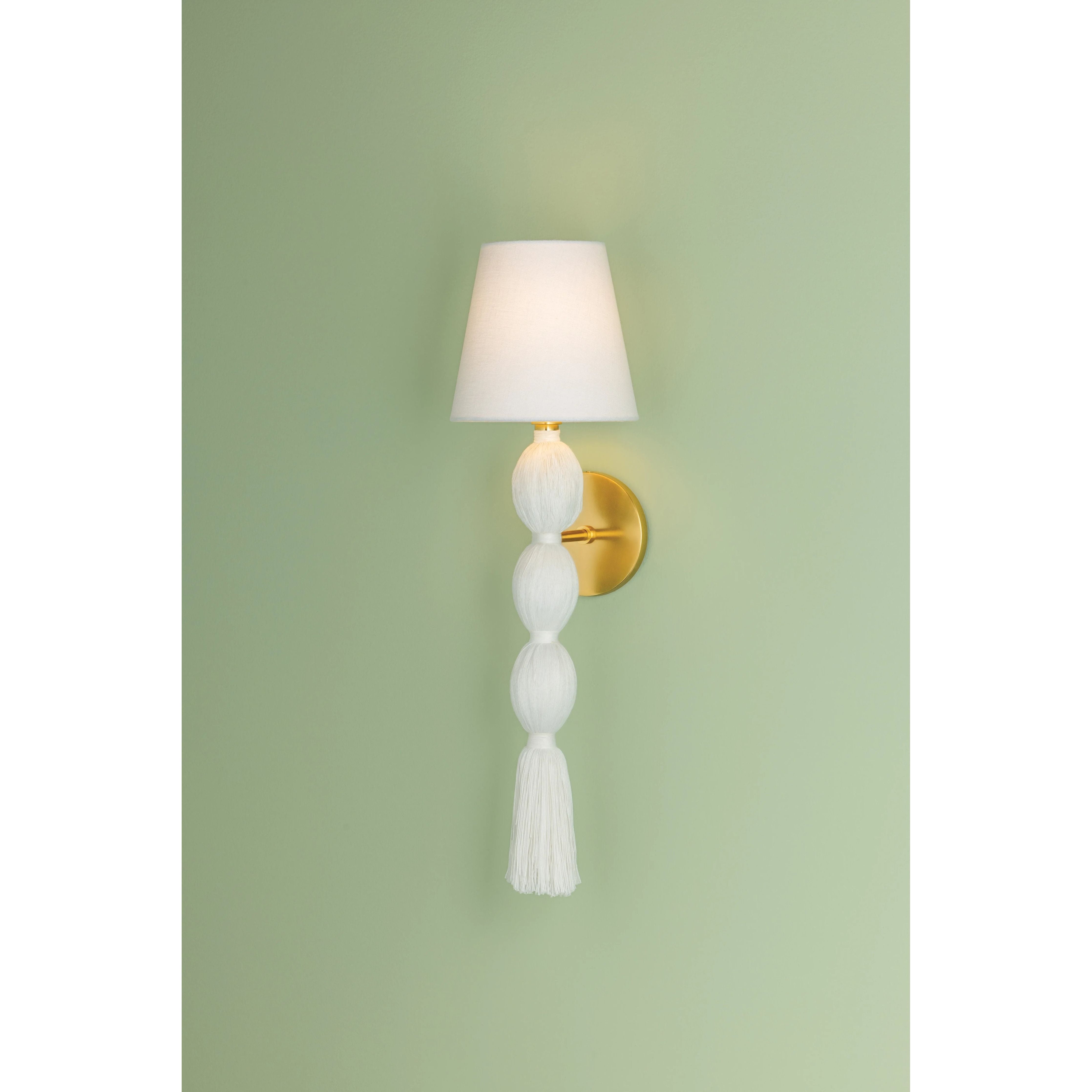 A celebration of authentic handicraft, the cinched silhouette of Indra resembles an elongated tassel. The cotton string and white linen shade create an all-over light, fresh appearance, accented by Aged Brass hardware at the neck. This single-light sconce serves as an artistic piece for small spaces in need of a spruce. Amethyst Home provides interior design, new home construction design consulting, vintage area rugs, and lighting in the Miami metro area.