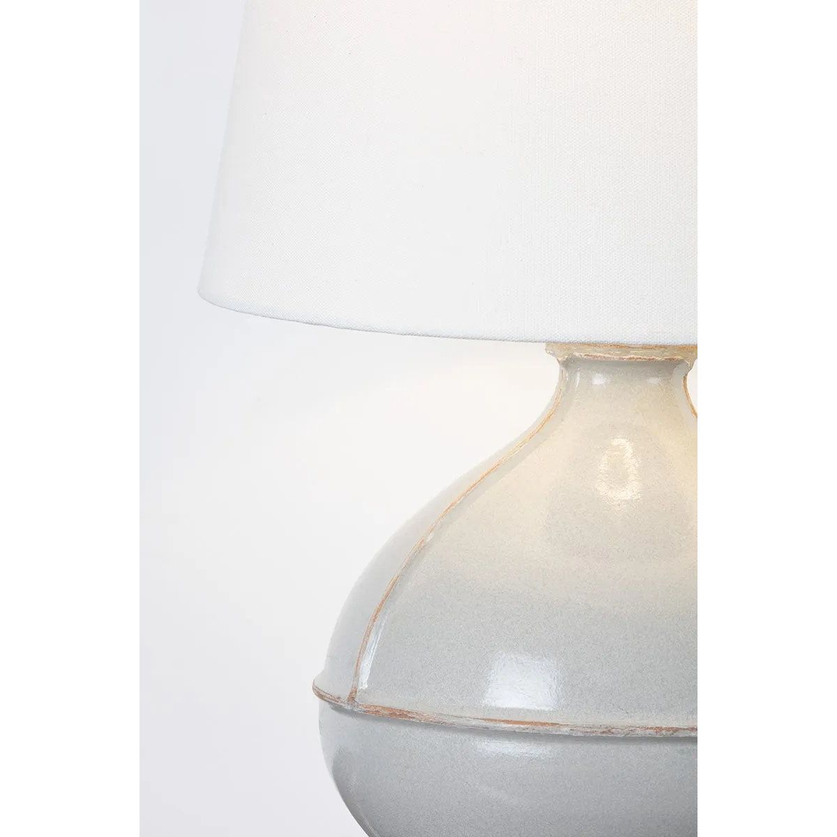 Inspired by rustic pottery, this table lamp's beautifully shaped base is crafted of pale sage ceramic giving it an earthy pale green tone. The off white linen shade pairs naturally and casts a soft glow. Raised seamlines and a reactive glaze that allows hints of the natural ceramic to peek through, give the fixture a hand-thrown, crafted feel. Amethyst Home provides interior design, new home construction design consulting, vintage area rugs, and lighting in the Miami metro area.