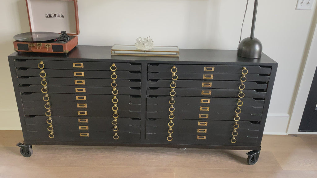 Crafted in vintage black mango wood and with brass hardware the Printmakers Console has been reconfigured to accommodate more space while retaining its classic form. There are 12 drawers for storage. This console is currently in the shop!  Size: 69"w x 13"d x 31"h Material: Mango Wood Finish: Vintage Black