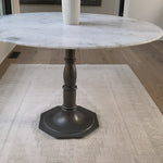 French-industrial meets bistro table. Detailed, 8-sided cast iron pedestal supports a dramatic white marble top with bull-nosed edge.  Overall Size: 36.00"w x 36.00"d x 31.00"h  Colors: Carbon Wash, White Marble Materials: Iron, Marble