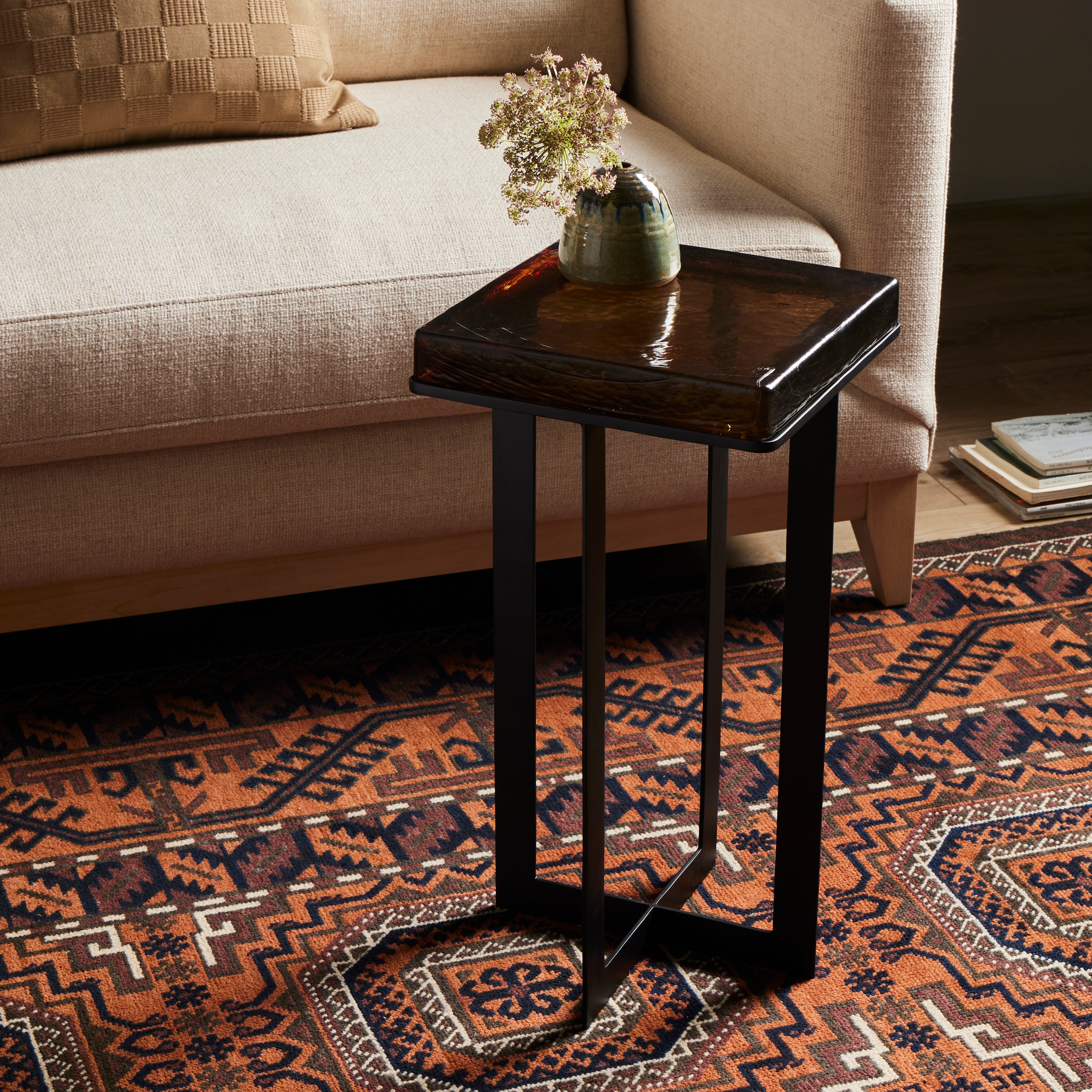 A cradle, angular base of black-finished iron supports a squared tabletop of hand-cast recycled glass in a smoky amber. Perfectly sized to keep your favorite drink or book within reach. Amethyst Home provides interior design, new construction, custom furniture, and area rugs in the Tampa metro area.