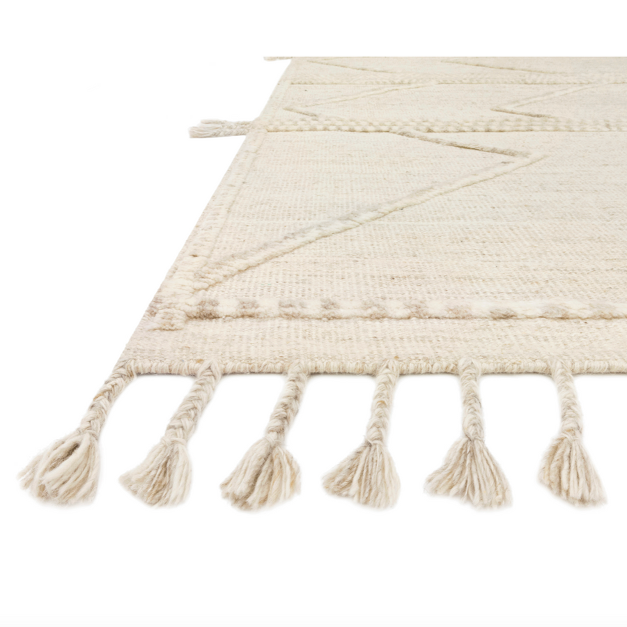 A new take on Moroccan style rugs, the Iman Beige/Ivory Rug from Loloi is hand-knotted of 100% wool pile by skilled artisans. The surface features linear and braided details, creating tonal variations that make each piece unique. Plus, each design is finished with a playful fringe.  Hand Knotted 100% Wool Pile IMA-05 Beige / Ivory
